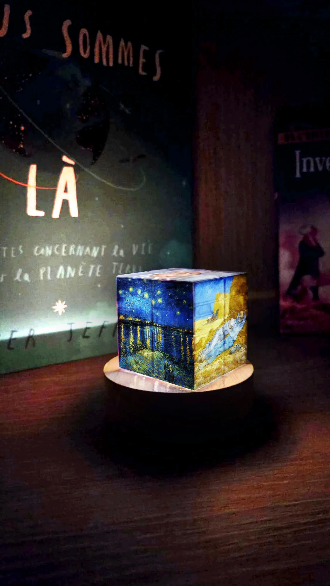 A Van Gogh illustrated nightlight glowing on its base in a dark room.